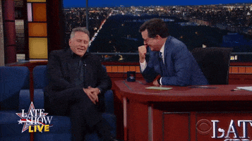 TV gif. On the Late Show, Paul Reiser mimics slapping his face with his hand while speaking, as Stephen Colbert leans on his deck, laughing.