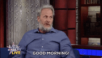 Celebrity gif. Jeff Daniels on The Late Show with Stephen Colbert sitting on the couch says loudly, "Good morning!"