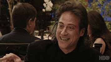 TV gif. Richard Lewis as Richard in Curb Your Enthusiasm. He's sitting at a restaurant and he's laughing hysterically, leaning back in his chair.