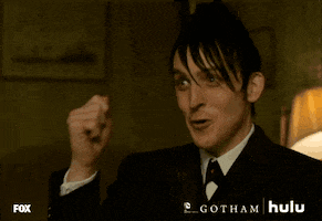 TV gif. Robin Lord Taylor as Oswald Cobblepot on Gotham pumps his fist, smiling at someone, then points his finger grinning at them.