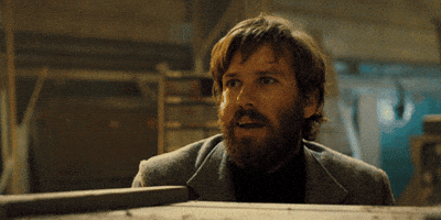 Movie gif. Cautious smile creeps across the face of Armie Hammer as Ord in Free Fire and he slowly raises a peace sign with his hand.