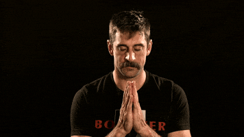 Video gif. Man has his hands in a prayer position under his chin. He has his head tilted down with his eyes closed. He then lifts his head and looks up at us, nodding slightly.