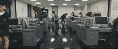 Music video gif. OneRepublic's Wherever I Go. A man in gray suit and tie, dances on a desk in an open floor plan office at night. Men and women in suits and skirt suits dance around the office as the camera moves with the action. 