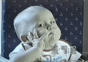 TV gif. AFV video of a bored-looking baby with food all over his mouth rests his head against his hand as he gives us the side eye. As a spoonful of porridge enters the frame, he opens his mouth for an uninterested bite.