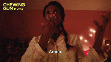 TV gif. Michaela Coel as Tracy in Chewing Gum, dressed in pajamas, holds her hand out and kisses her other hand, then reaches forward to place her kissed hand on a poster of Beyonce next to a poster of Jesus.