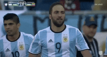 Sports gif. Gonzalo Higuain points at a teammate with both fingers as he walks toward him and then they do a double high-five.