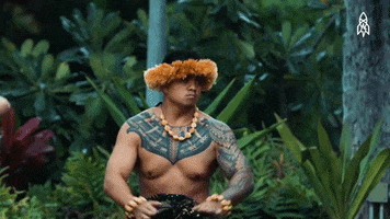 Video gif. Performing a hula dance, a tattooed man makes raised hand motions and slowly leans very far backward.
