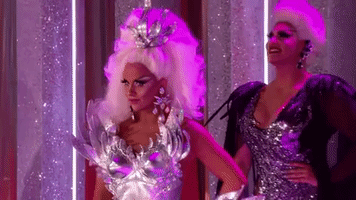 Reality TV gif. A contestant about to perform on RuPaul's Drag Race sharply looks over and gasps in shock at someone they've seen.