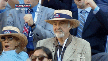 Sports gif. Wearing a tan suit and a US Open boater hat, Sean Connery sits in the stands amongst other sharply dressed fans. He proudly pumps his fist, and his face reveals that he had no doubts whatsoever.