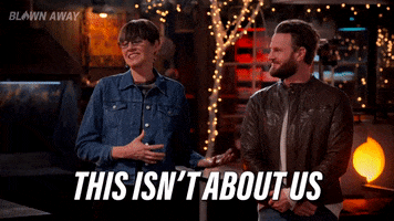Reality TV gif. Katherine Burns and Bobby Berk, the judges of Blown Away, stand in front of the contestants chuckling. Katherine says, "This isn't about us. This is about you." 