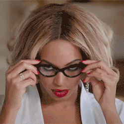 Celebrity gif. Beyonce, wearing red lipstick and dark eye makeup, slowly takes off a pair of black eyeglasses and stares at the camera with a sultry, sexy look. 