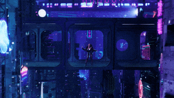Music video gif. From the video for Thought About That, Noa Kirel stands in the center of a futuristic bridge walkway between two tall buildings, while flying cars drive below and digital screens light up around.