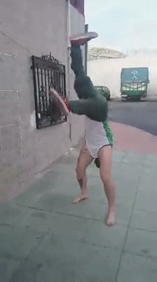 Video gif. A person wearing shoes on their hands and pants on their arms appears to be spinning around and walking on their hands, which are actually their feet.