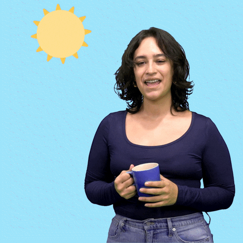 Video gif. Woman holding a mug in front of a baby blue background leans to the side, smiling as she waves with fluttering fingers. She says, "Buenos dias," in Spanish, which appears as text beneath a spinning cartoon sun.