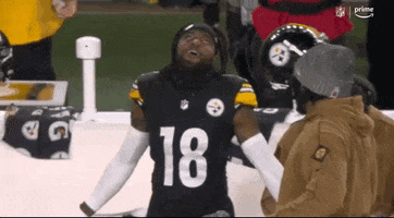 Sports gif. Diontae Johnson of the Pittsburgh Steelers stands on the field with his hands up to the heavens as he smiles and looks up in wonder.