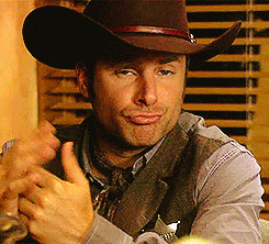 TV gif. Actor James Roday in Psyche wearing a cowboy outfit. He holds out his hands and shrugs like he's casually confused and not worried about it.