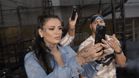 An animated gif of two people holding their phones out, filming something.