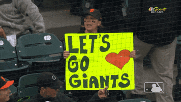 Sports gif. An excited MLB fan holds a giant yellow poster that reads "Let's go Giants!"