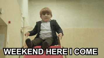 Video gif. A stout young boy in a suit rides down a small slide, crashing with a bounce at the bottom. Text, "Weekend, here I come."
