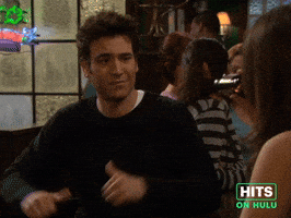 Sponsored GIF. Josh Radner is sitting in a bar talking to a friend, mid conversation he takes a beat to focus the attention on himself by leaning back, pointing his two thumbs back at himself and comedically proclaims himself “this guy” as if delivering a punch line from a joke