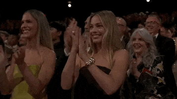 Oscars 2024 GIF. Margot Robbie, seated at the Oscars, applauds prominently.