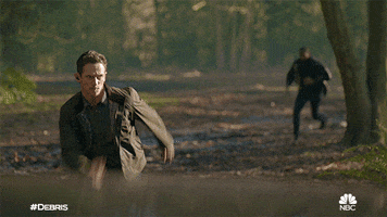 TV gif. A scene from the tv show Debris. A man runs fast through the woods. He has a determined look on his face. Another man is chasing after him. 