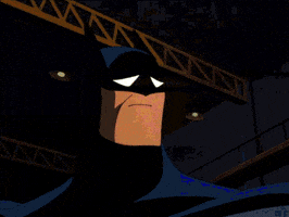 Cartoon gif. Batman turns to look down in the shadows as he shakes his head despondently and the scene goes dark.