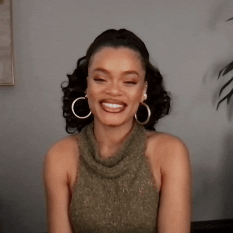Tonight Show gif. Andra Day smiles widely at us, and waves with both hands. She then claps her hands together and clasps them tight.