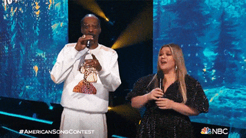 TV gif. Snoop Dogg and Kelly Clarkson are on American Song Contest. Snoop says something that makes Kelly crack up and she guffaws while putting an arm out.