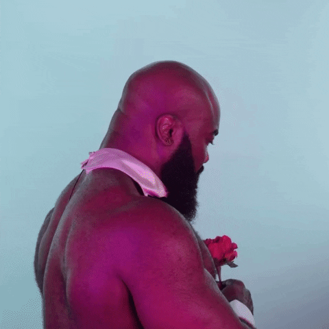 Video gif. A muscular bald man with a full beard, wearing only a bowtie collar turns towards us, holding a rose. He says with a smile, “It’s only Tuesday.”