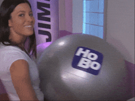 Video gif. Brunette woman holds an exercise ball between her hips and a wall and she aggressively humps into the ball, which bounces back and forth.