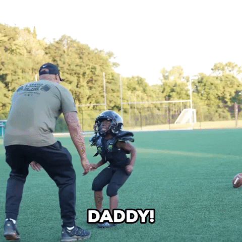 Video gif. Man on a football field leans down to pick up a young player who runs over to him, lifting him up and giving a big sweet hug. Text, "Daddy!'