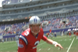 Movie gif. Zoom in on Rhys Ifans as Nigel Gruff in the Replacements wearing a football uniform and standing in the middle of a football field. He leans forward as if ready to run and he grins widely at us. 
