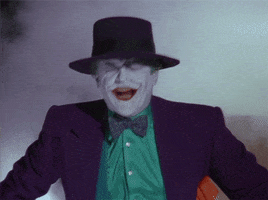 Movie gif. While fog billows around him, Jack Nicholson as The Joker in Batman tips his head back in hysterical laughter.