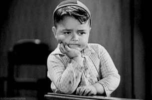TV gif. In a black and white scene, George McFarland as Spanky from The Little Rascals holds his head in one hand and drums restlessly on a desk with the other.