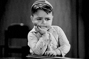 TV gif. In a black and white scene, George McFarland as Spanky from The Little Rascals holds his head in one hand and drums restlessly on a desk with the other.