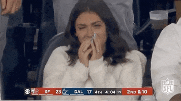 Sports gif. Girl in the bleachers of a Dallas Cowboy and San Francisco Forty niners game sobs with red eyes. She covers her mouth with her hands as she cries.