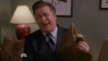 TV gif. Alec Baldwin as Jack on 30 Rock laughs boisterously as he covers his face with a pillow. 