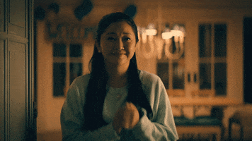 TV gif. A scene from To All the Boys Always and Forever. Appreciating a tender moment, a smiling Lana Condor as Lara Jean clutches her hands together and rests them under her chin.