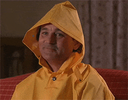 Movie gif. Bill Murray as Bob Wiley in What About Bob sits on a couch with a yellow raincoat on with the pointy hood over his head. He giggles, shrugs, and then says, “K.”