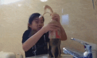 Video gif. An uncomfortable young girl tries to hold onto an overflowing bottle of Diet Coke.