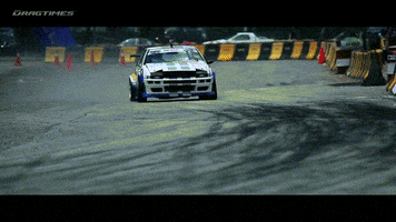 Video gif. A racing car that’s slightly damaged in the front drifts and drives away, dust blowing behind it. 
