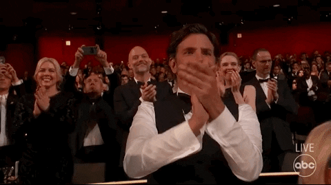 Celebrity gif. Bradley Cooper finely dressed for the Academy Awards claps as he gives a standing ovation in the audience. 
