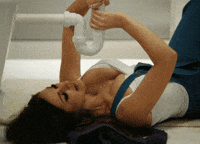 Video gif. A very beautiful woman lays on the floor below a PVC pipe under a sink. Her breasts are falling out of her white tank top. She suggestively pulls the pvc pipe with both hands and then looks at us while she struggles with the pipe. 