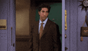 Friends gif. David Schwimmer as Ross stands near a door and looks annoyed as he gestures with his fists as if saying screw you. 
