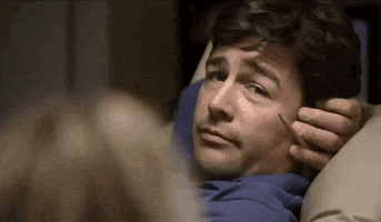 TV gif. Kyle Chandler as Eric Taylor leans back in a reclining chair. His arm is behind his head and in his same hand he holds a pencil. He looks over at Connie Britton as Tami Taylor with an ernest smile and then winks. 