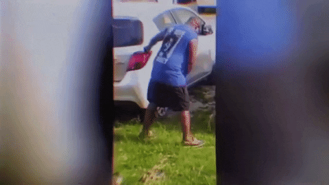 Video gif. A man staggers forward, trying to grab onto the side of a car. He then leans over too far and ends up falling down on his stomach. The video is glitching. 