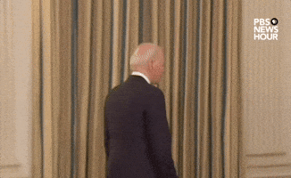 Political gif. Joe Biden turns around slowly and smiles over his shoulder.