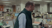 Video gif. Interior of an office. Tim Robinson makes an uncomfortable wincing face as he turns and faces the camera.