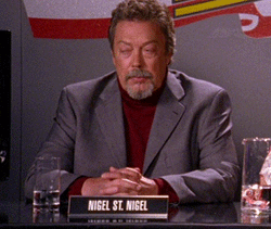 TV gif. Tim Curry as Nigel St Nigel on Psych sits on a judge's panel and looks frustrated, putting his head in his hands.